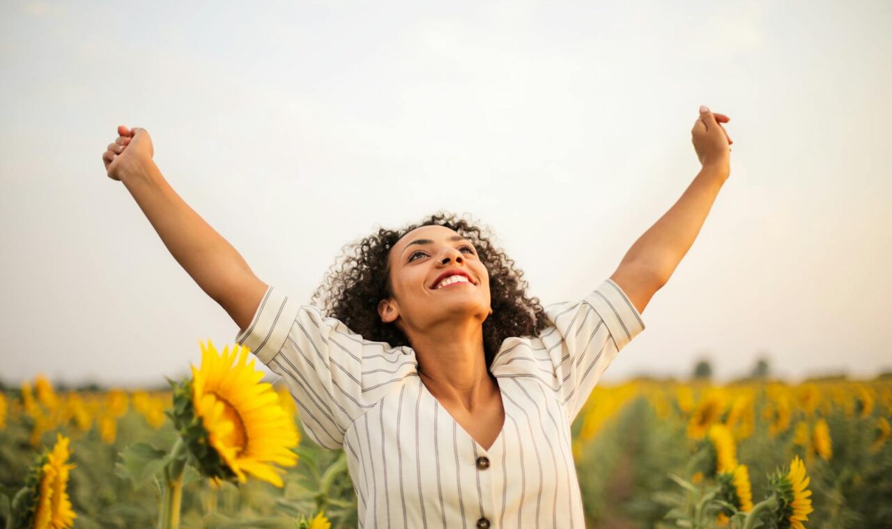 Joyful woman with arms raised in a sunflower field, embracing freedom and happiness.