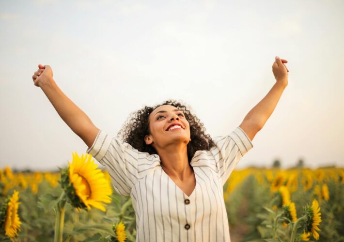 Joyful woman with arms raised in a sunflower field, embracing freedom and happiness.