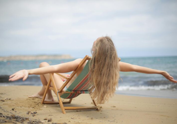 A woman enjoys a relaxing moment on a sandy beach, arms outstretched, embracing the summer vibes.