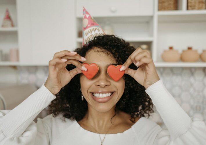 Joyful woman with heart-shaped candies celebrates her birthday indoors.