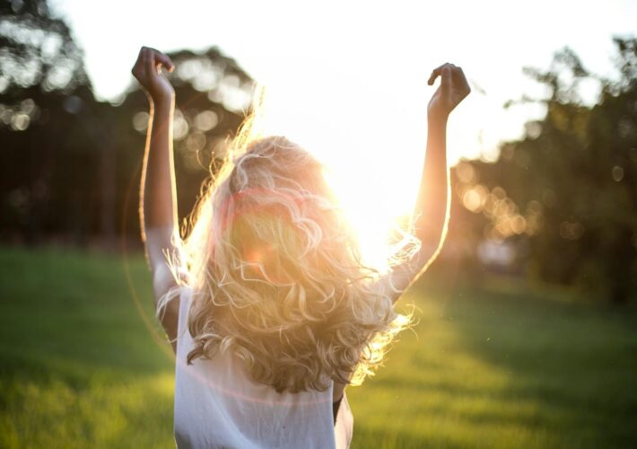 A woman with outstretched arms celebrates the sunset in a grassy field, capturing the essence of freedom and joy.