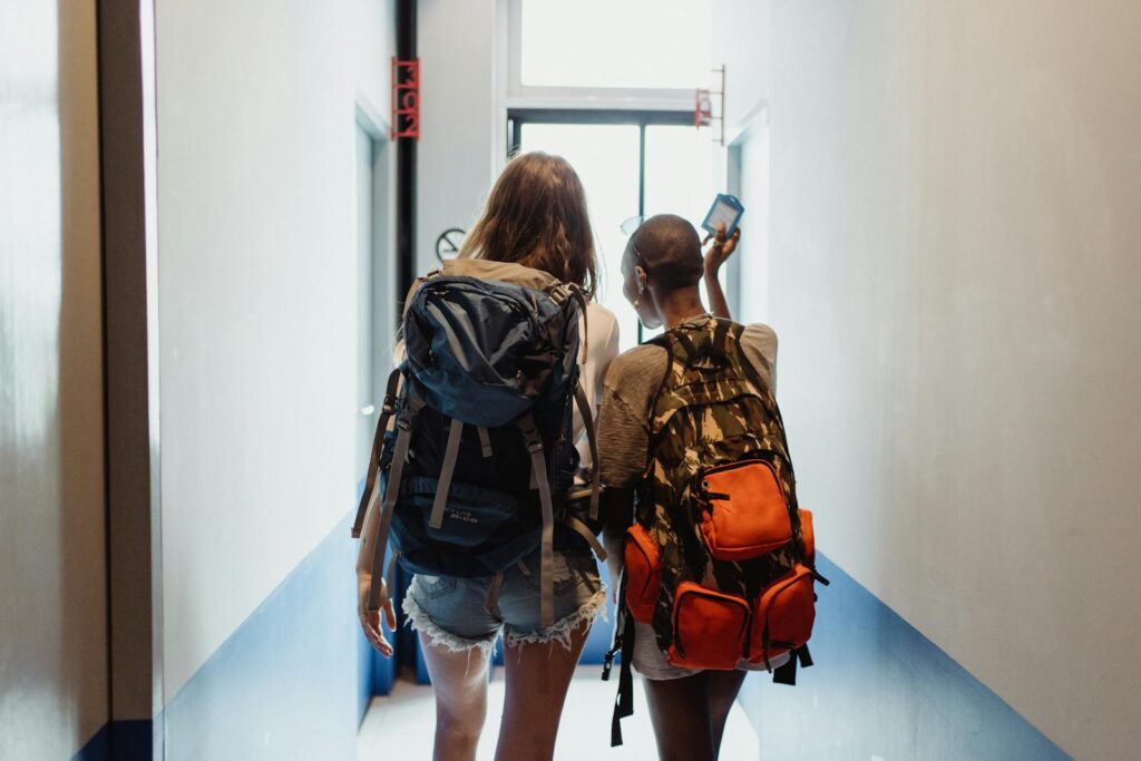 Two women with backpacks walking through a hallway, suggesting travel friendship.