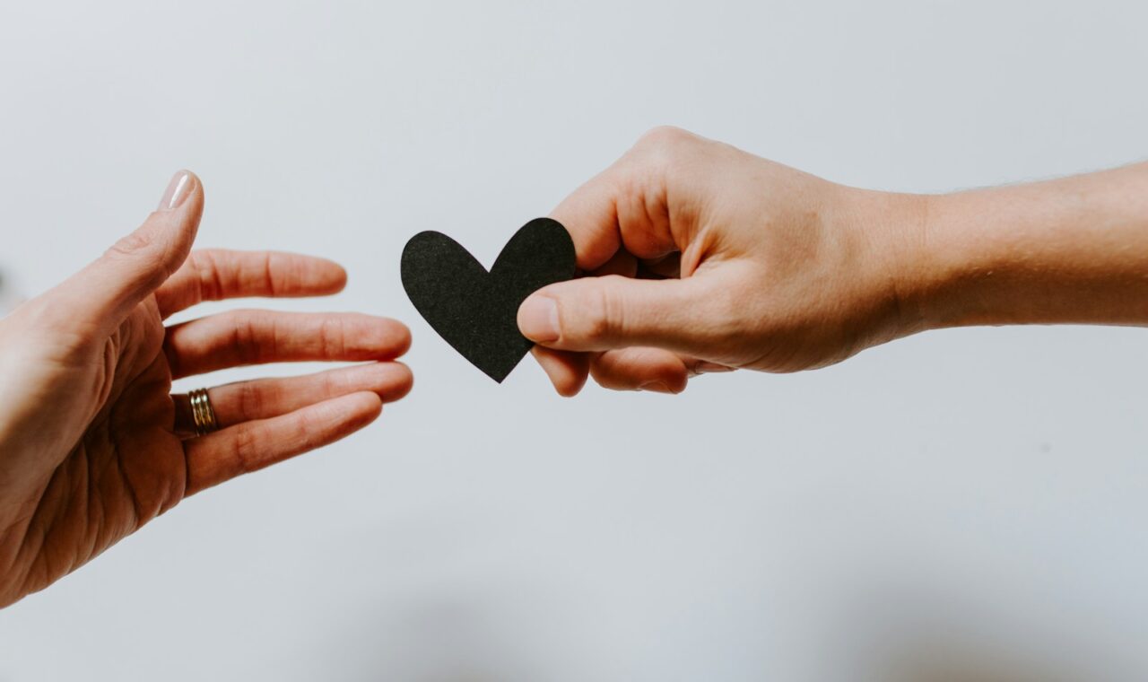 person reaching black heart cutout paper